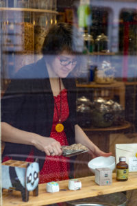 View of a young woman through a shop window. She fills cereals in a white bowl, detail from an unwrapped shop. View of a young woman through a shop window. She fills cereals in a white bowl, detail from an unwrapped shop.